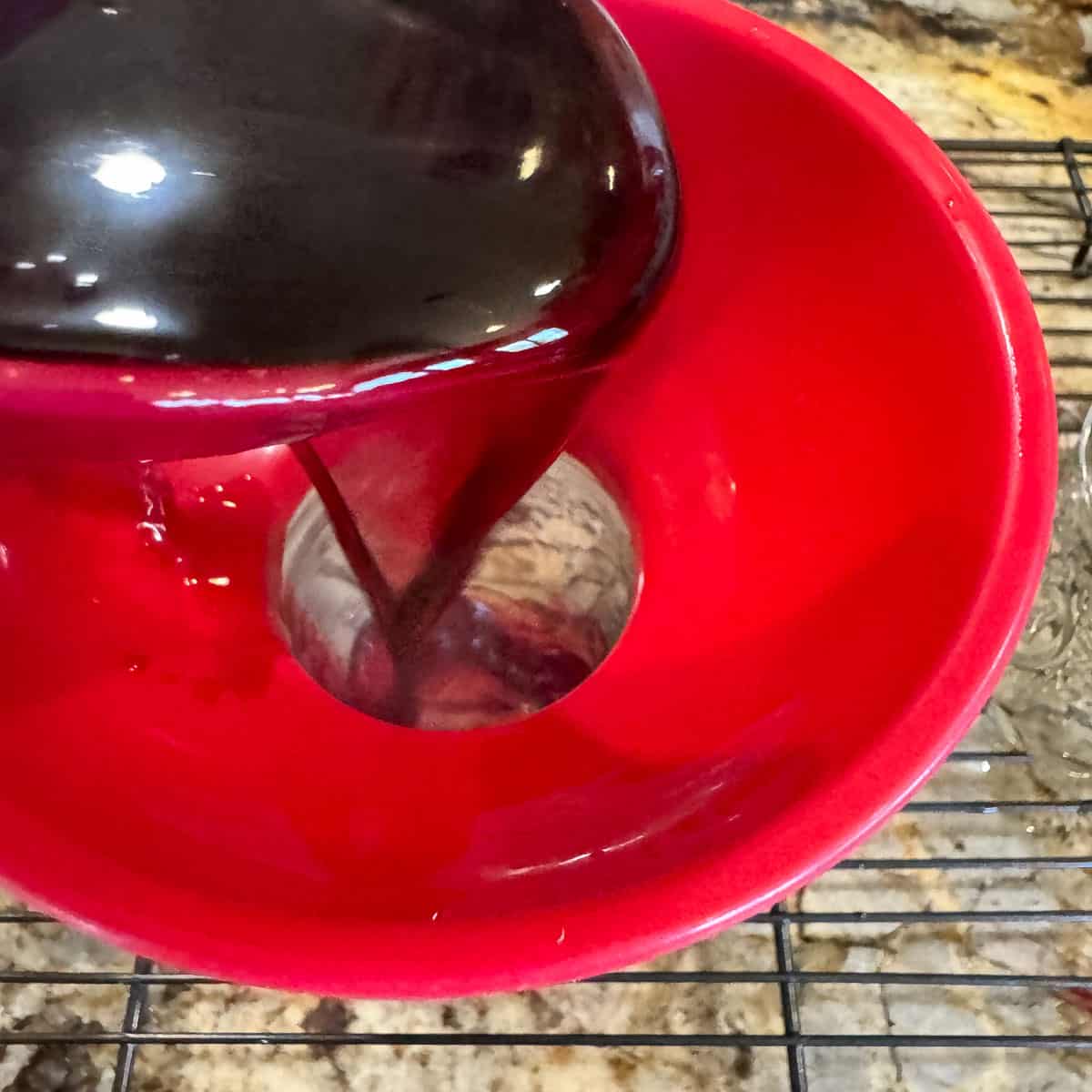ladling oregon grape jelly into jars through a red funnel.