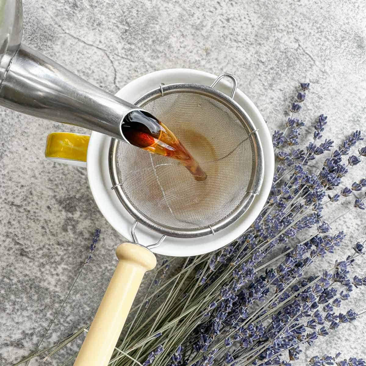 pouring tea in tea cup, through a strainer, with lavender in the background .