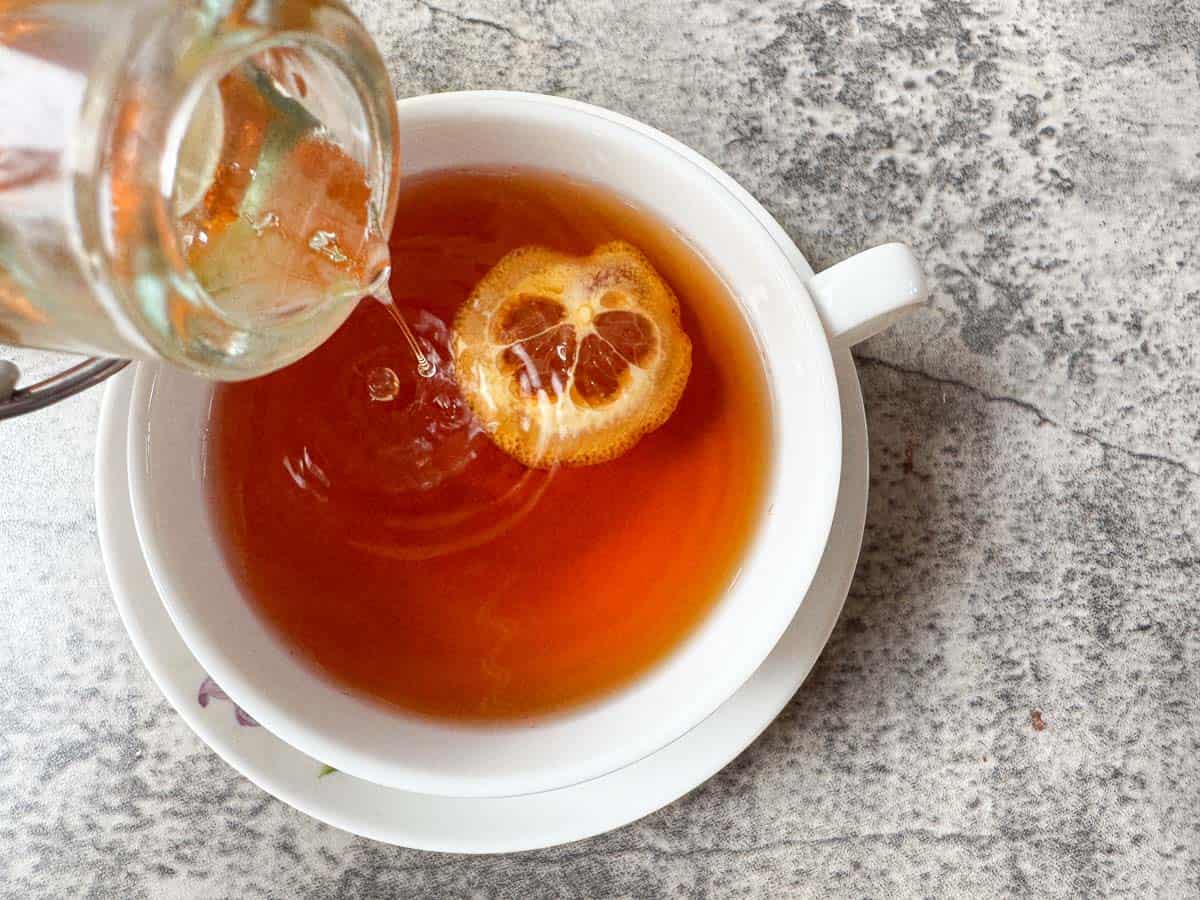 syrup being poured into a cup of tea.