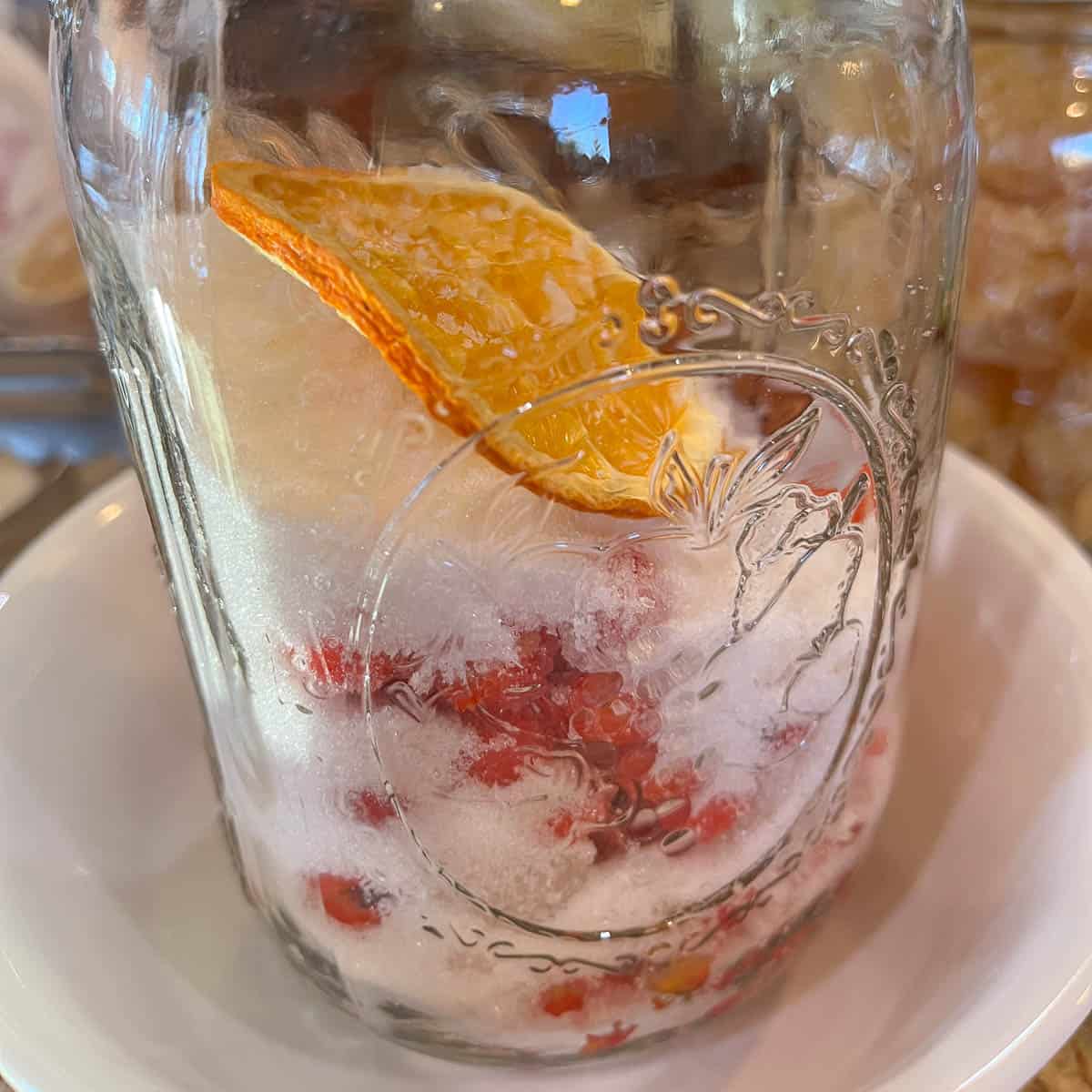 a jar with sugar and rowanberries, and orange slice.