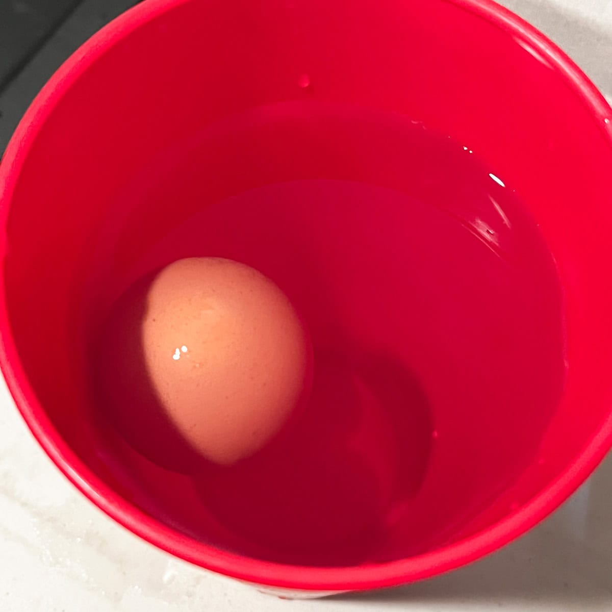 egg floating to top of a red cup with water. 