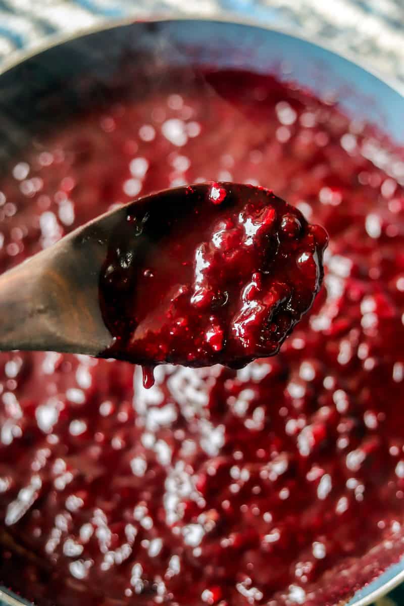 a spoon of huckleberry chutney over a pot of chutney. 