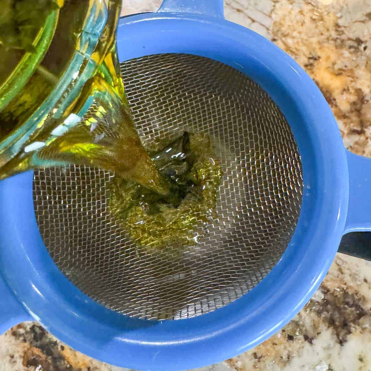straining comfrey oil through a blue strainer.