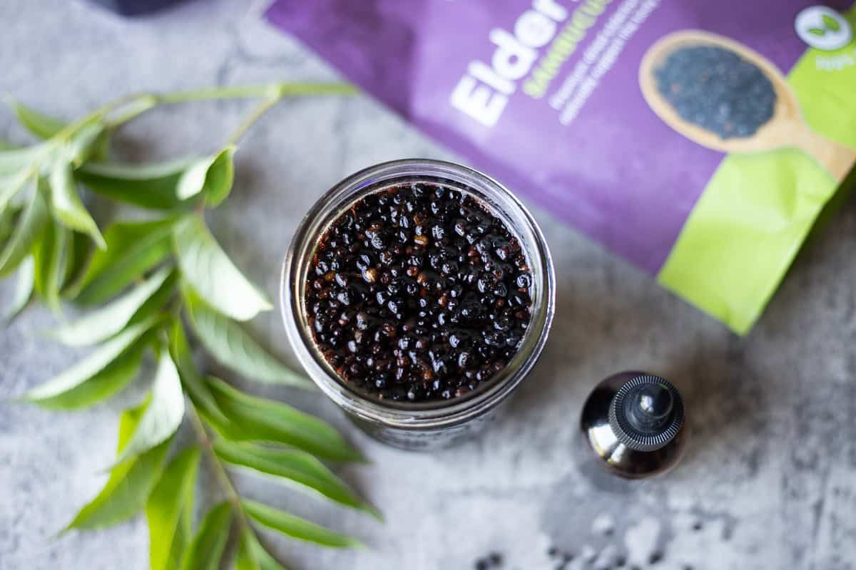elderberry tincture in a jar with elderberry leaves, and a bag of elderberries next to it. 