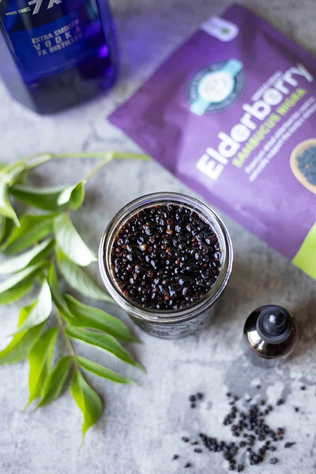 elderberry tincture in a jar with elderberry leaves, and a bag of elderberries. 