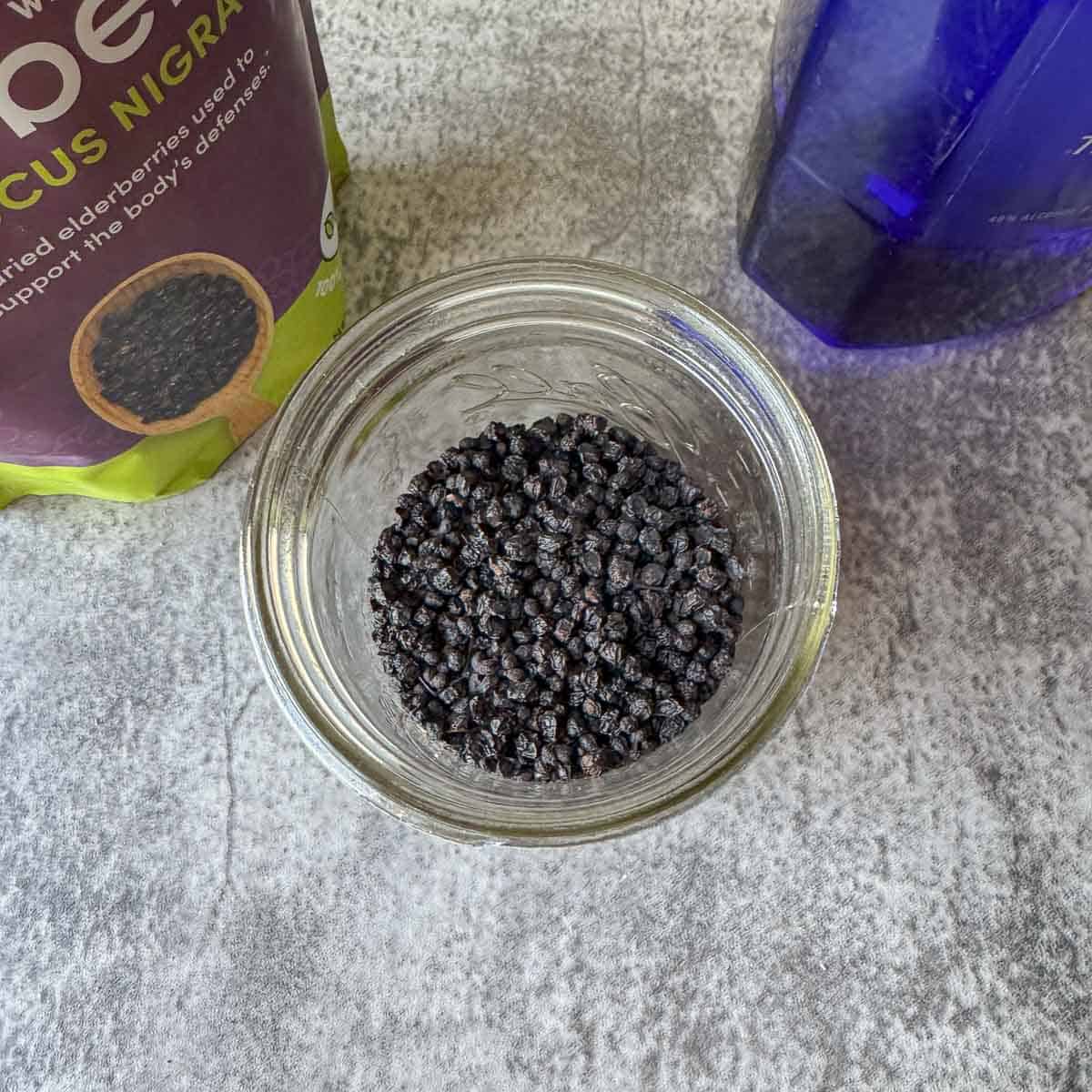 elderberries in a jar with more in a bag and a bottle of vodka. 