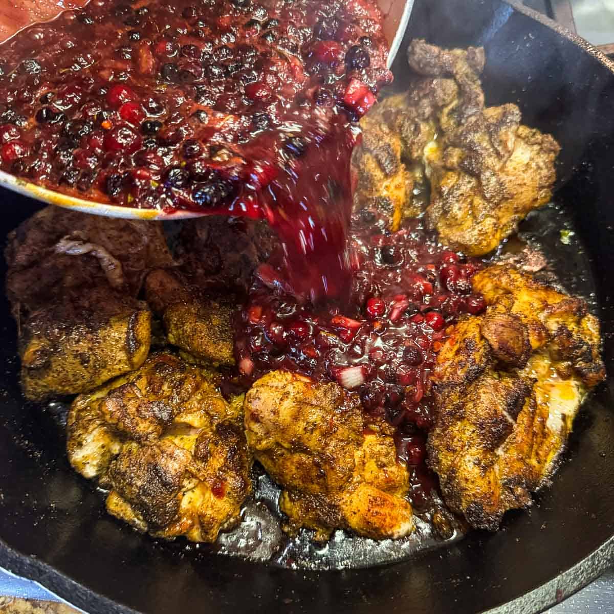pouring huckleberry sauce over chicken.