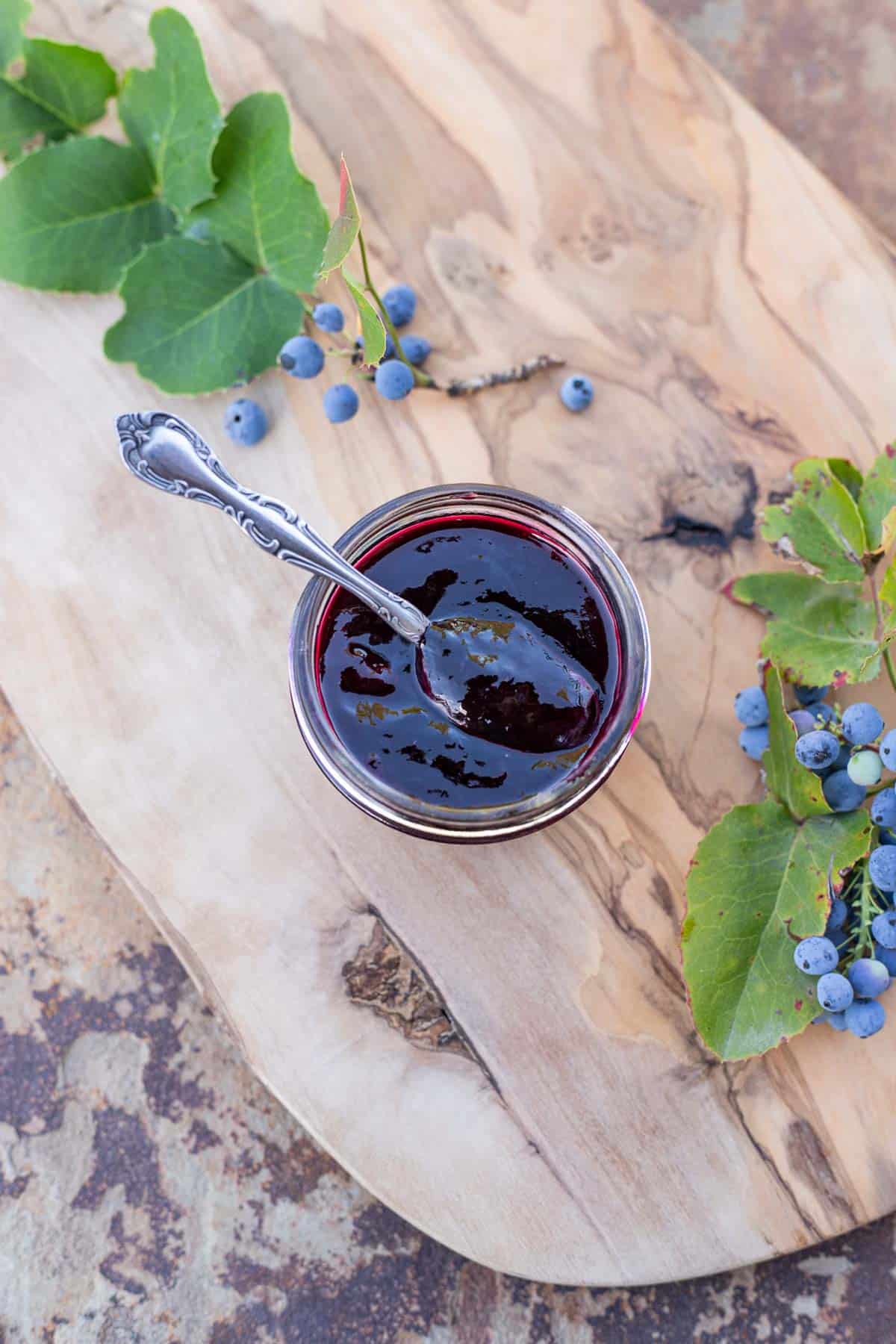 Oregon grape jelly with a spoon in it and oregon grape around it.