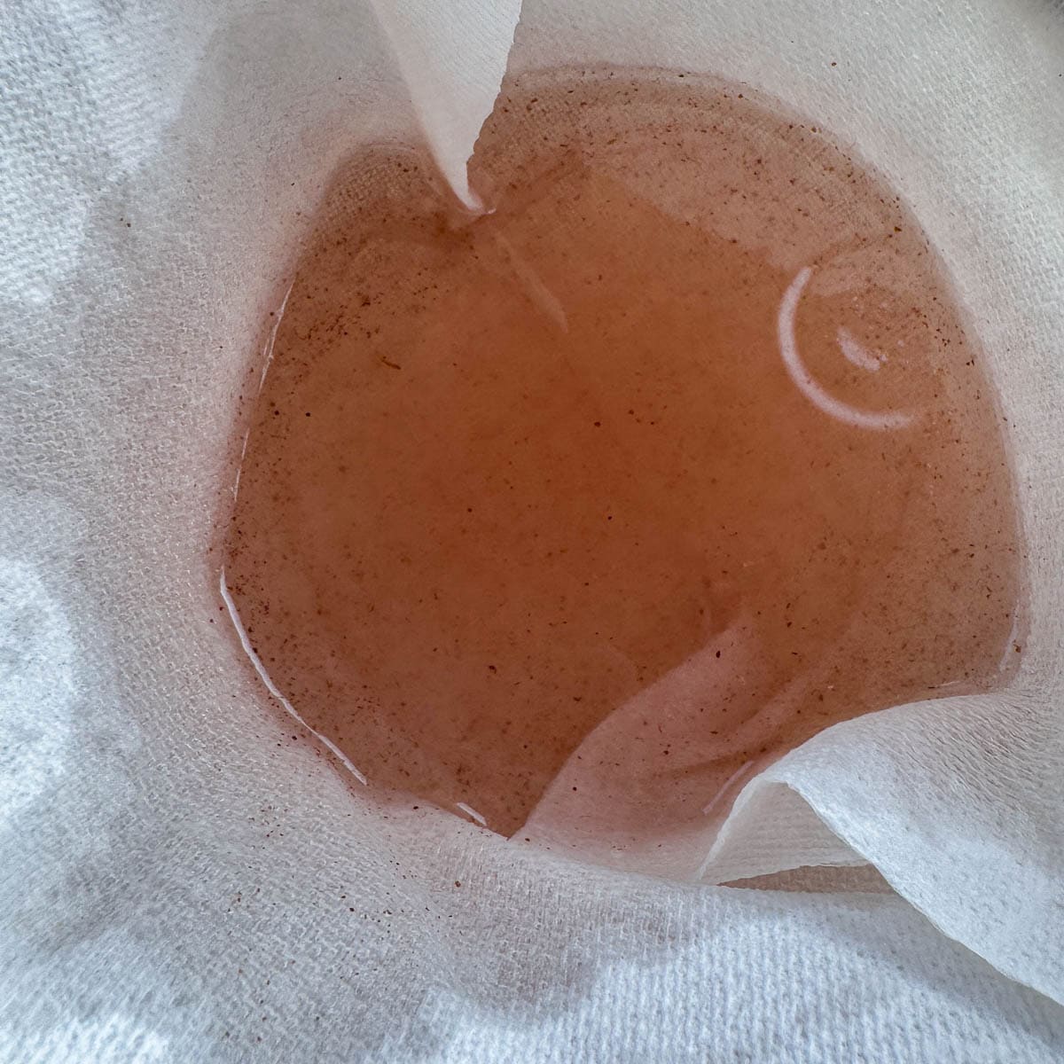 sumac lemonade being s trained through a paper towel lined strainer. 