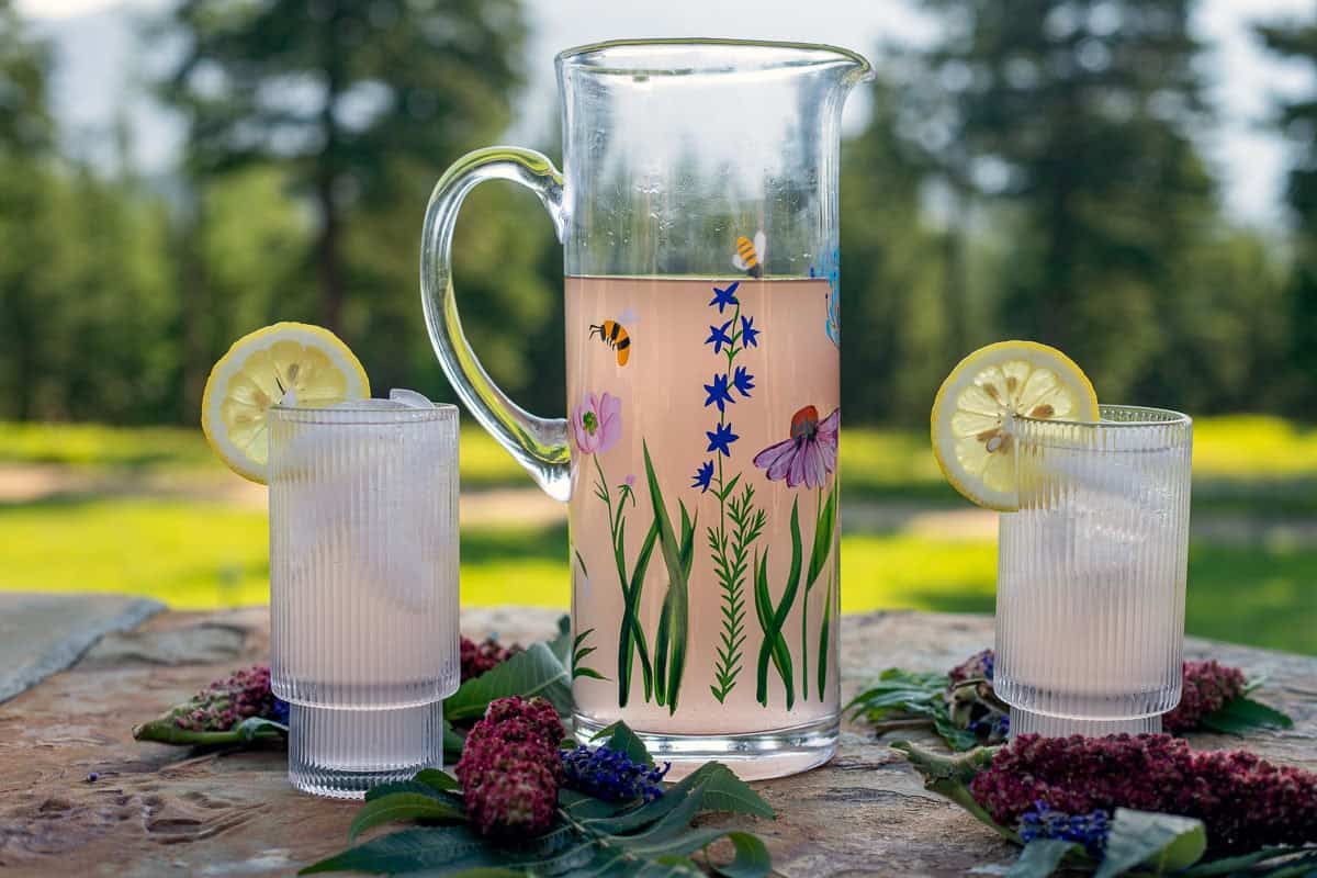 sumac lemonade in a pitcher with 2 glasses.