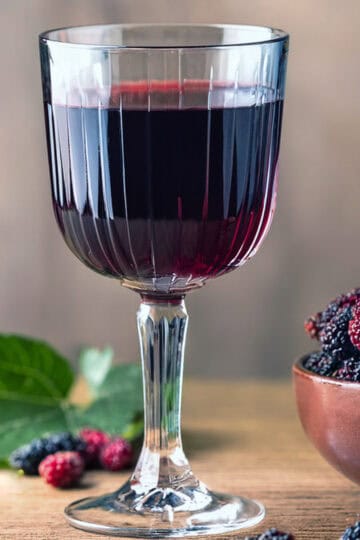 mulberry wine in a glass with mulberries around it.