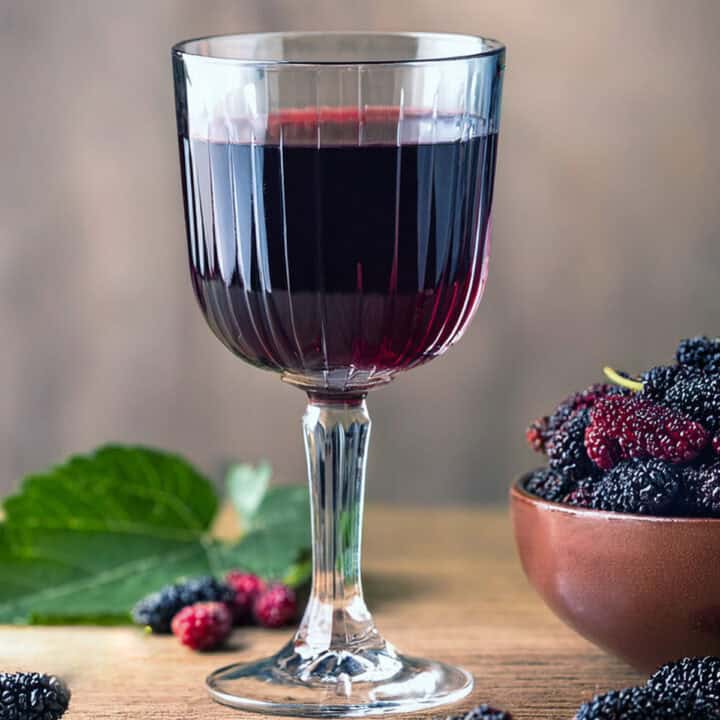 mulberry wine in a glass with mulberries around it.