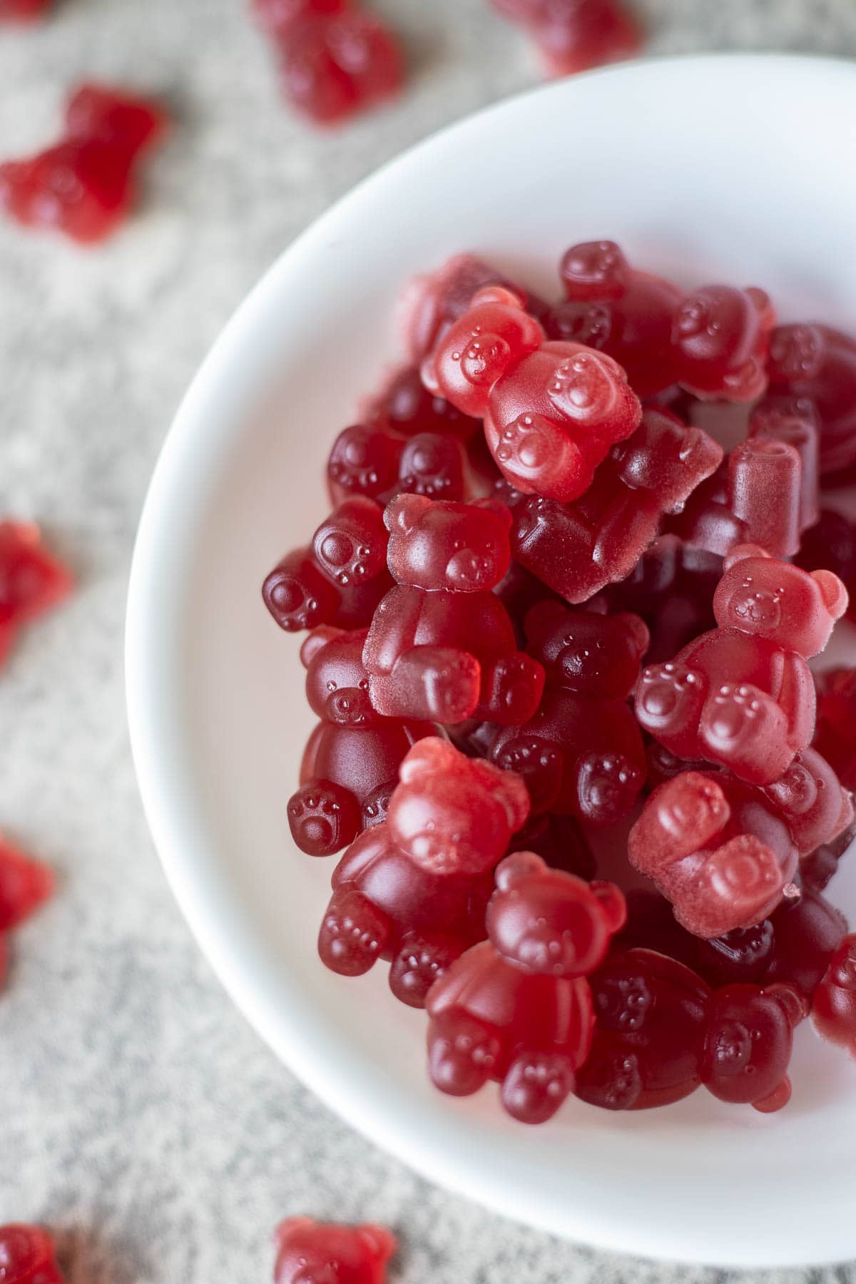 elderberry gummies in a white bowl with more gummies around it.