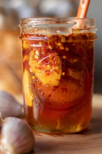 a jar of fermented garlic honey with garlic bulbs around it.