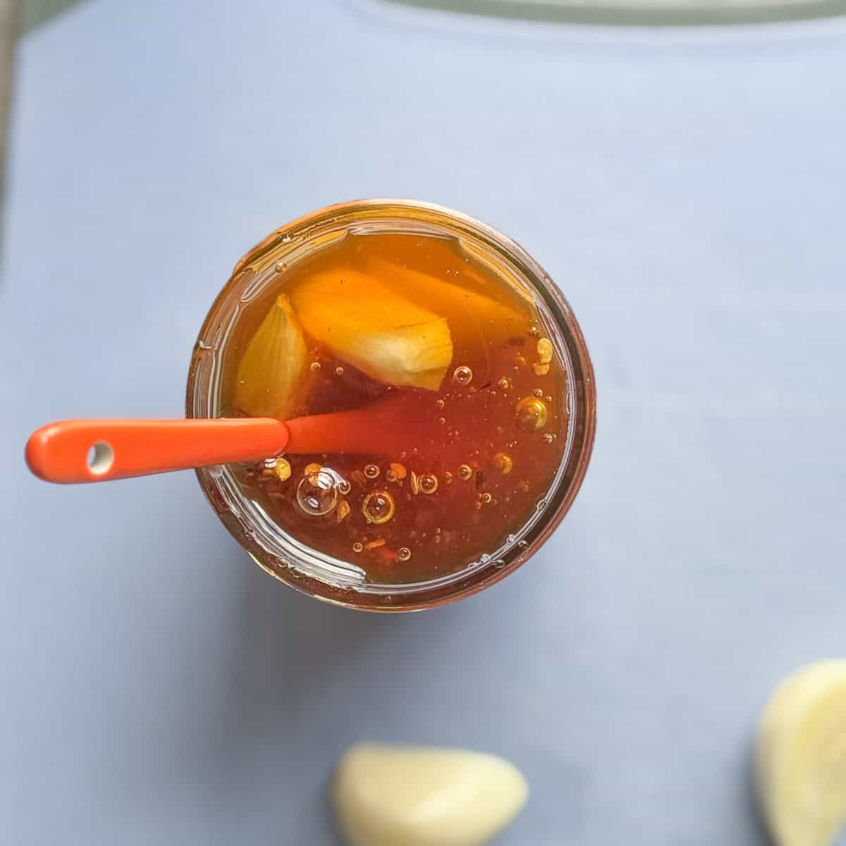 fermented garlic and honey jar with an orange spoon sticking out of it and garlic cloves next to it.