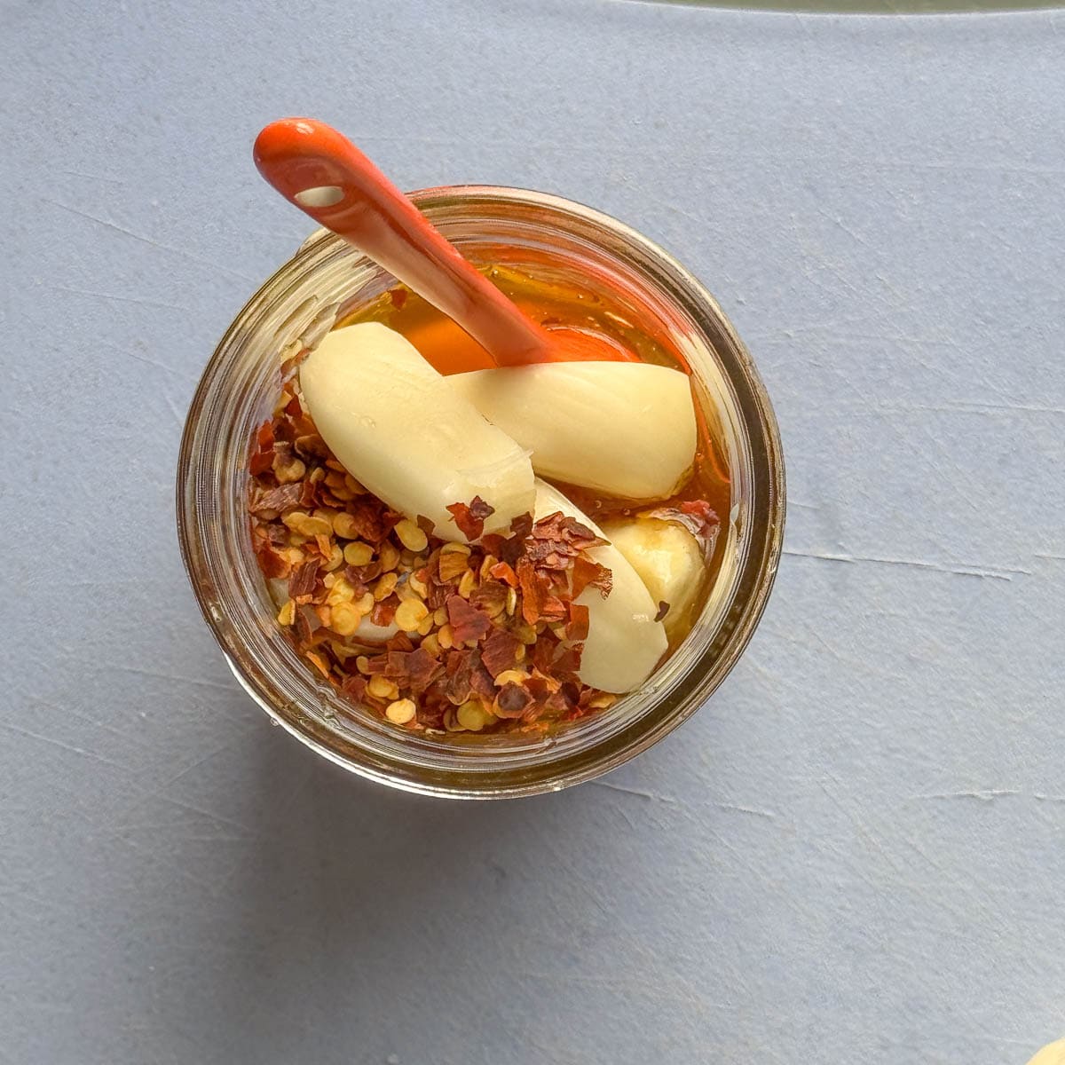 a small jar with garlic cloves, crushed red pepper, and an orange spoon.