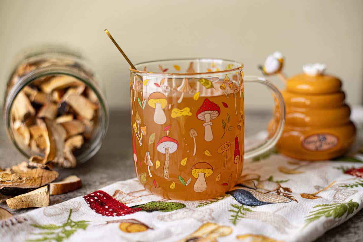 red belted polypore tea with more dried mushrooms spilling out of a jar and honey jar in the background.