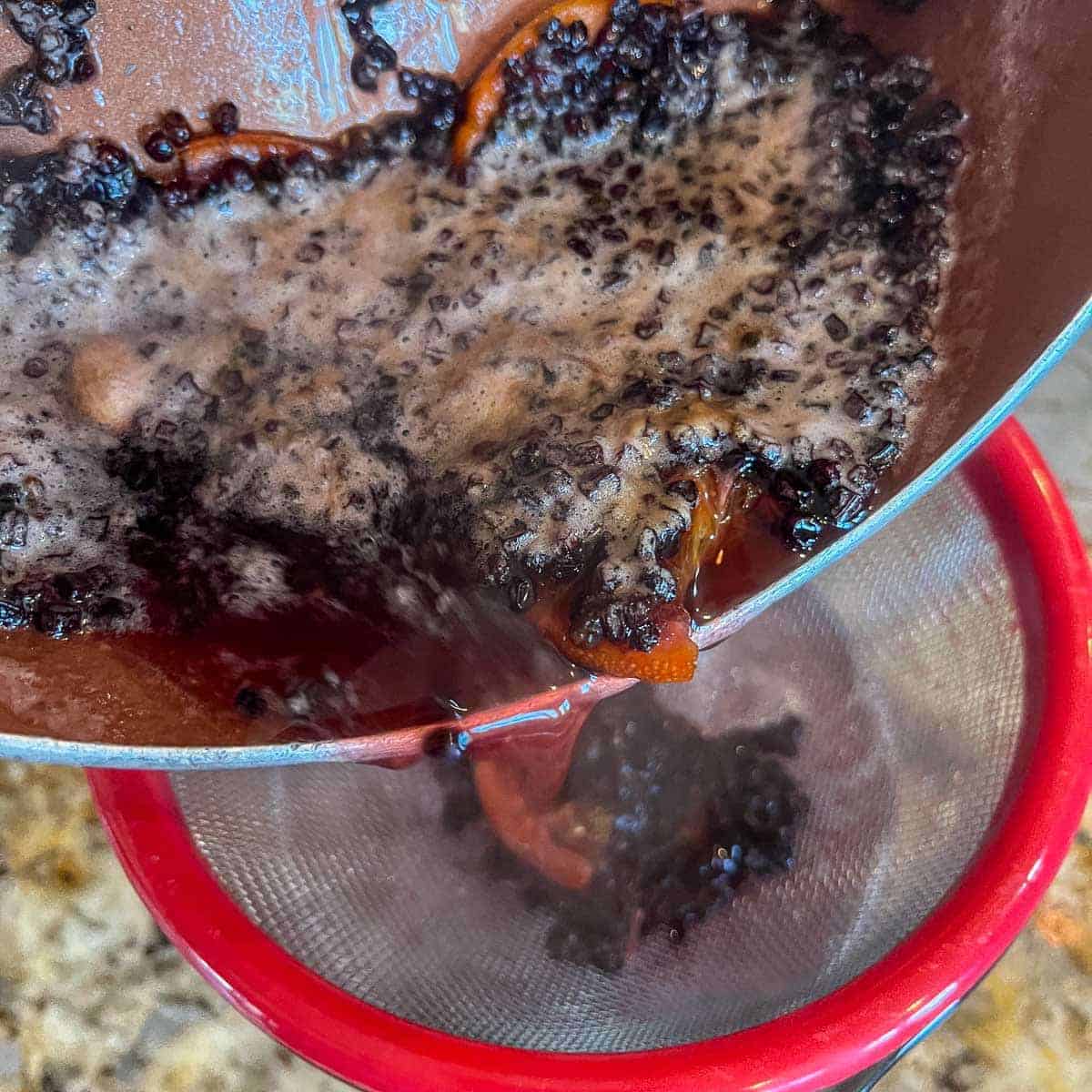 straining elderberry shrub into a jar.