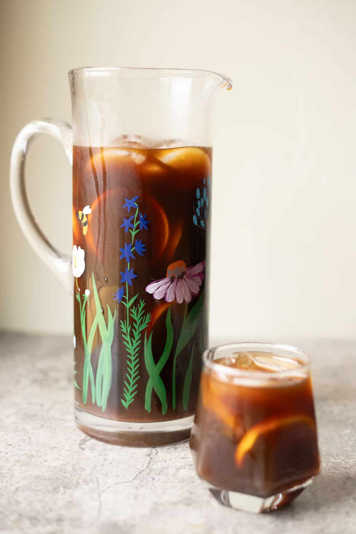 switchel (hay maker's punch) in a jar decorated with flowers and a glass in front of it.