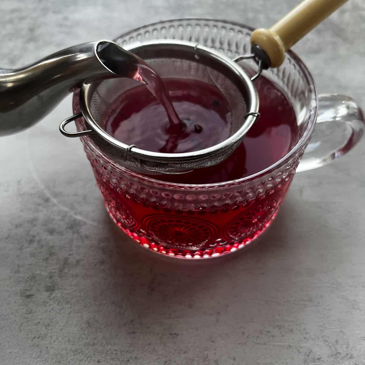 straining black elderberry tea into a tea cup.