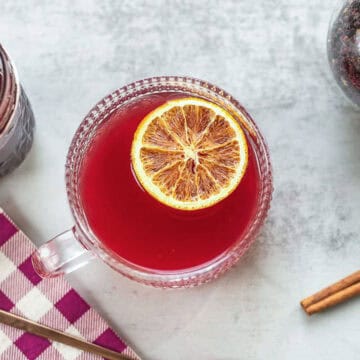 elderberry tea in a cup with orange slice, cinnamon stick, and elderberry syrup.