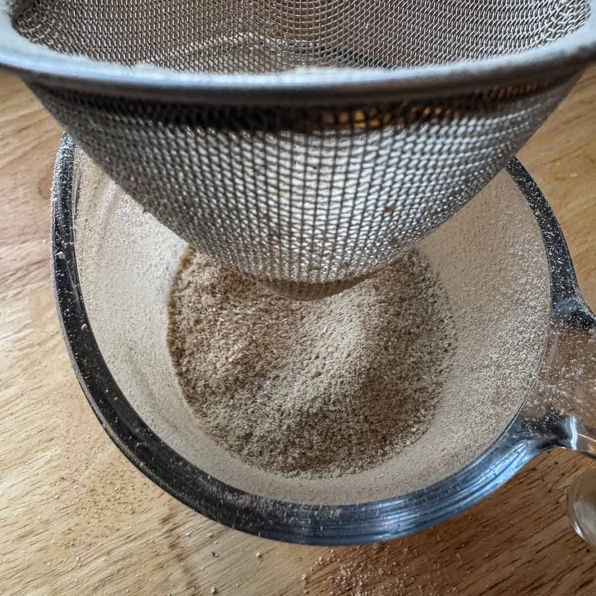 sifting powder through a sieve into a cup