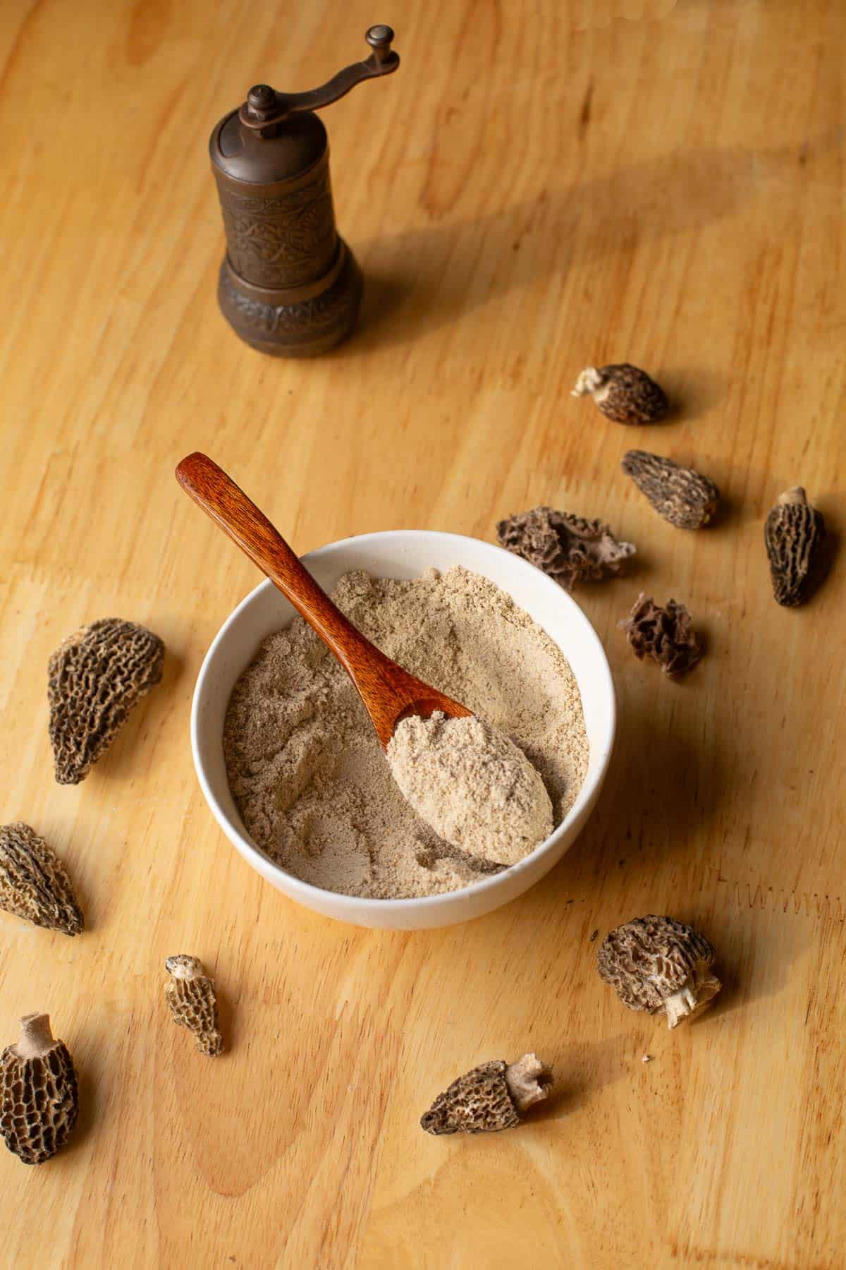 umami mushroom seasoning in a bowl with a wooden spoon and morels scattered around it.