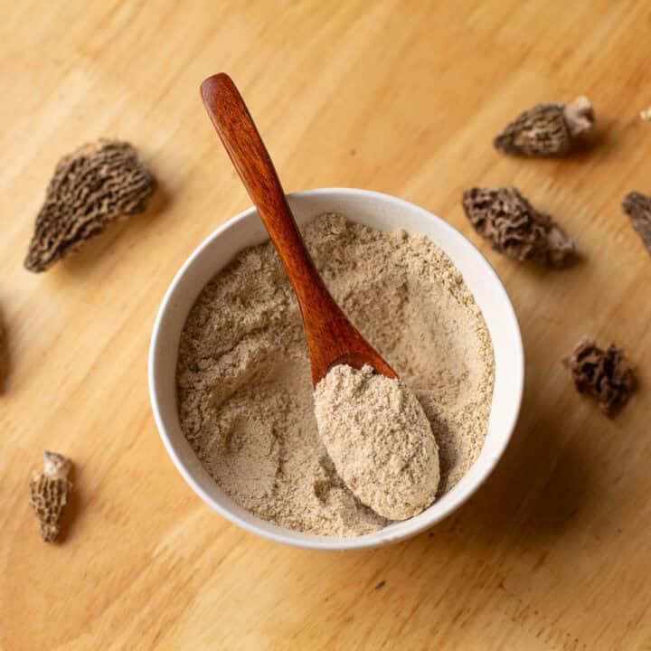 mushroom seasoning in a bowl with a wooden spoon and morels scattered around it.