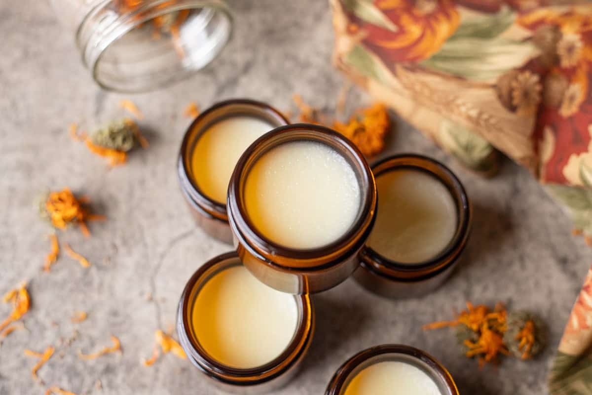 tallow balm in jars with dried calendula flowers around it spilling out of a larger jar and a colorful napkin. 