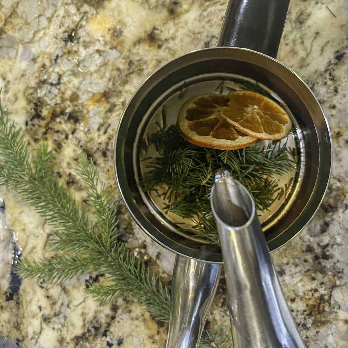 puouring hot water over pine needles and orange slices in a tea pot