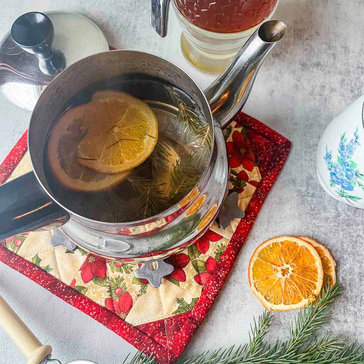 pine needle tea in a tea pot with orange slices and pine needles around it