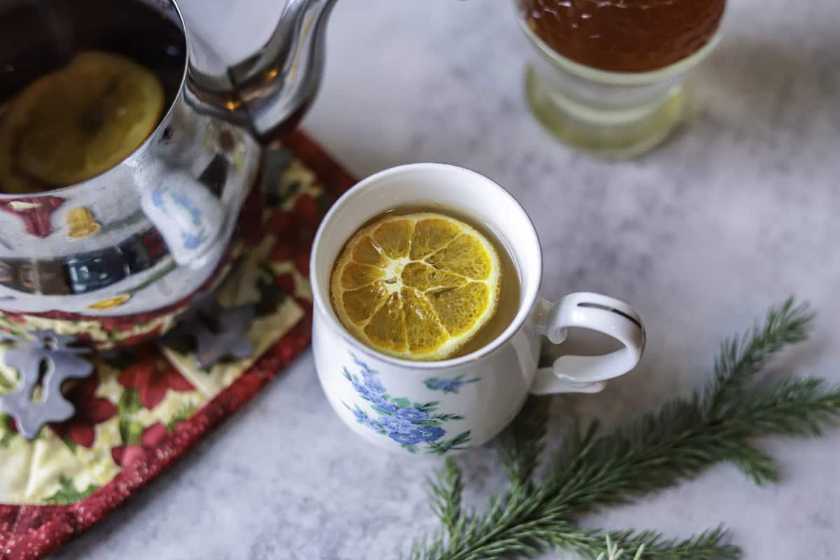 pine needle tea in a cup with an orange slice, next to a tea pot of tea