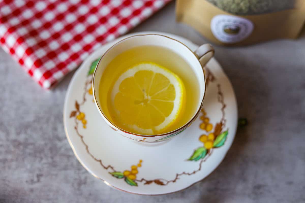 a cup of mullein tea with a slice of lemon and a red and white checkered napkin