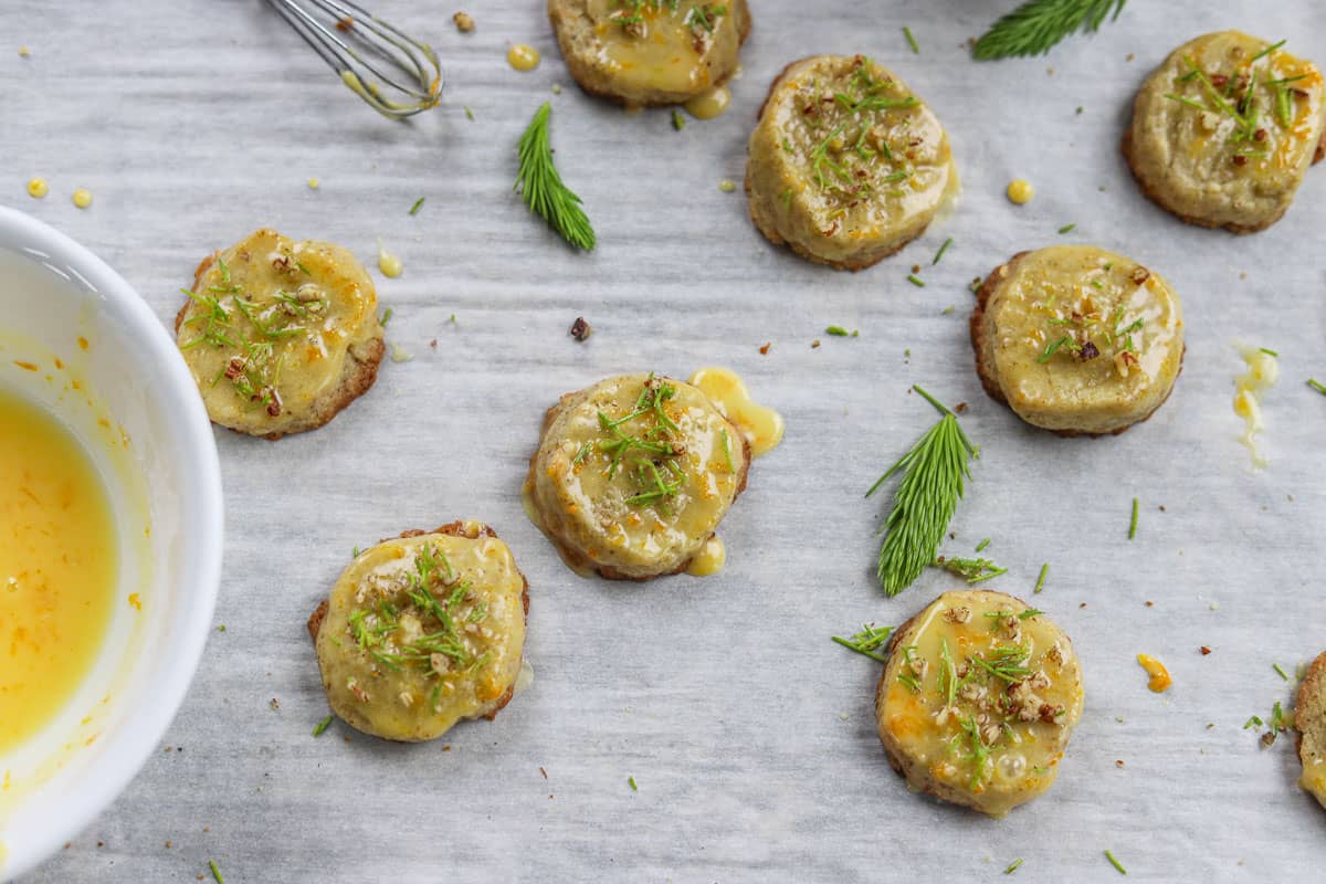 spruce tip cookies with orange glaze and spruce tips with white bowl.