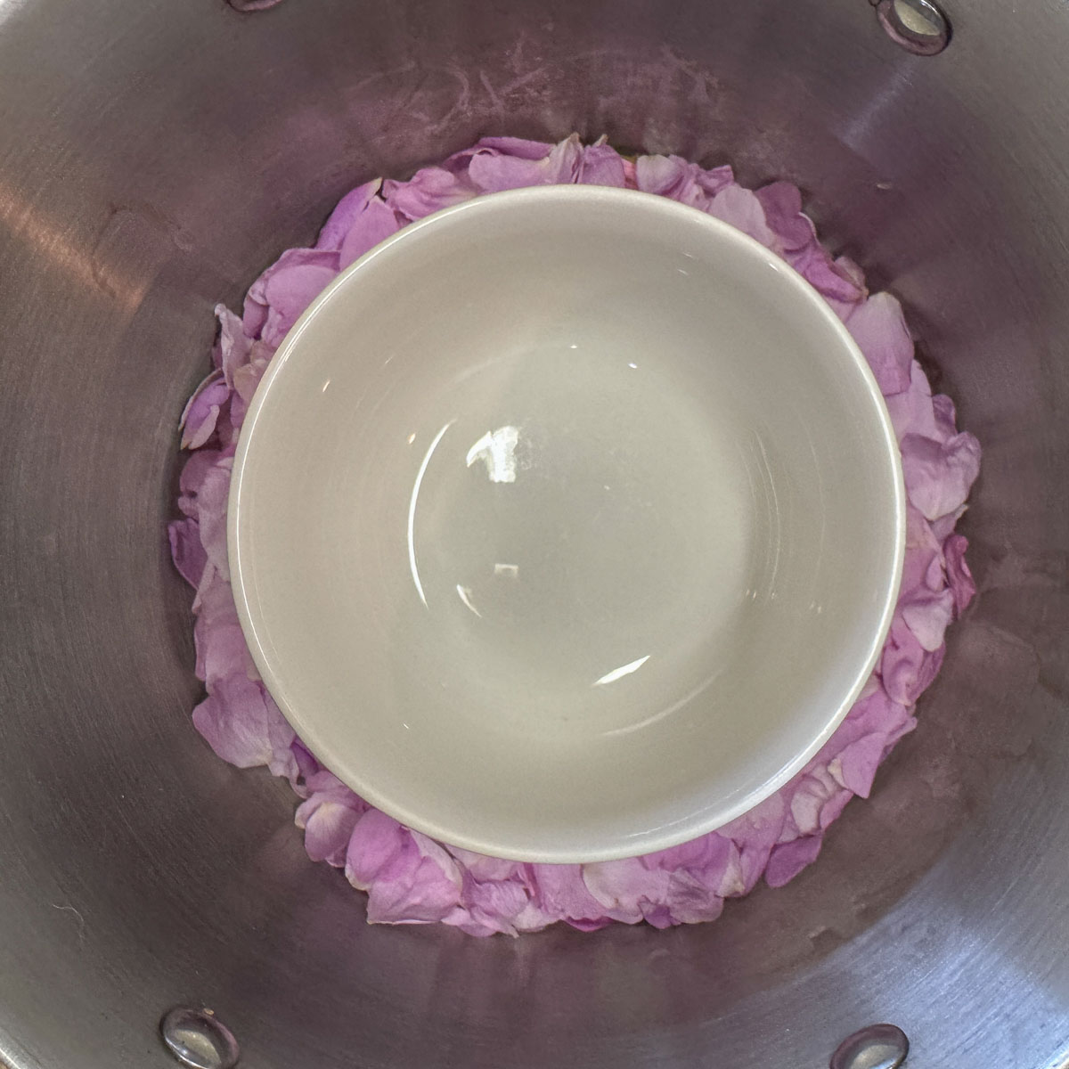 a white bowl in a silver pot with pink rose petals around it