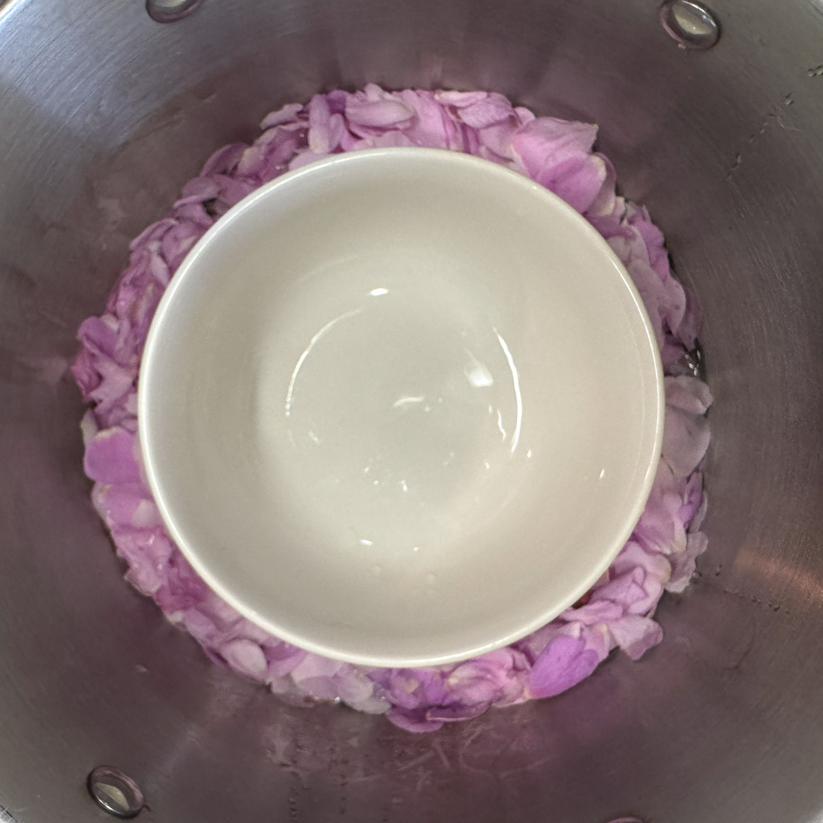 a white bowl in a silver pot with pink rose petals and wate around it