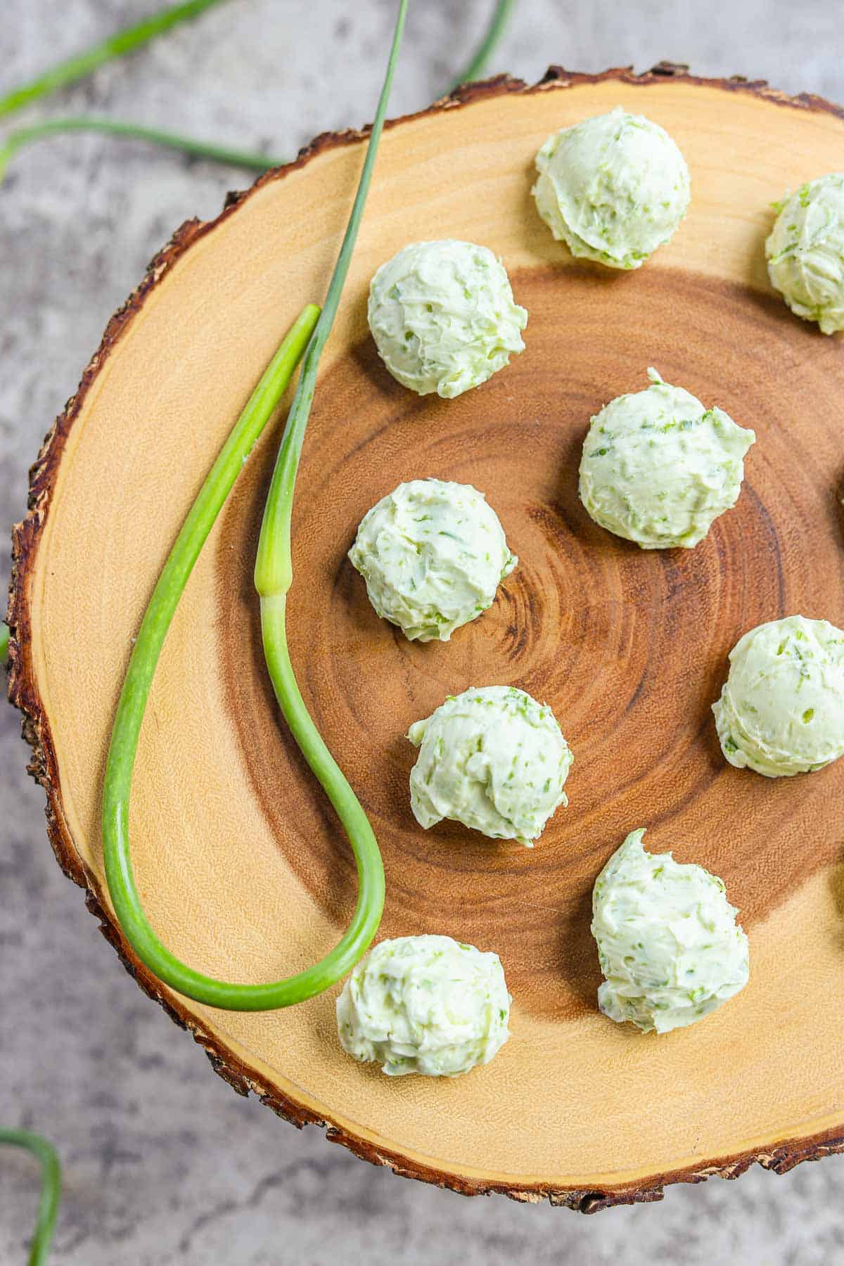 frozen rounds of garlic scape butter on a wooden board with a garlic scape next to them