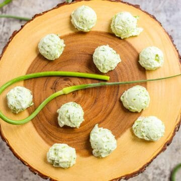 garlic scape butter on a wooden round board with a garlic scape in the center and more around it