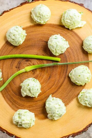 garlic scape butter on a wooden round board with a garlic scape in the center and more around it
