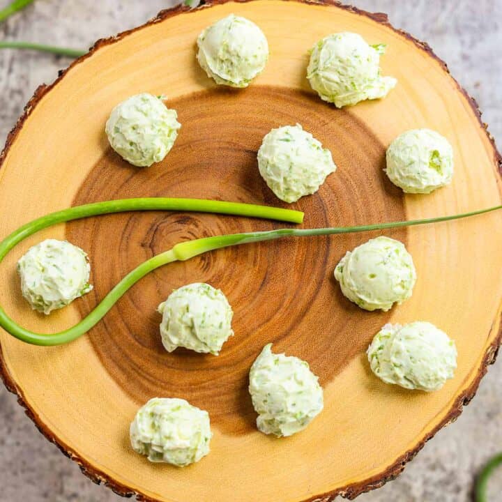 garlic scape butter on a wooden round board with a garlic scape in the center and more around it