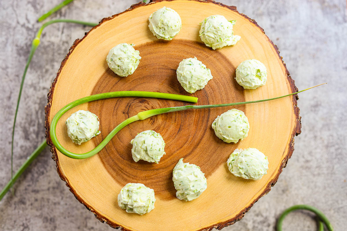garlic scape butter on a wooden round board with a garlic scape in the center and more around it