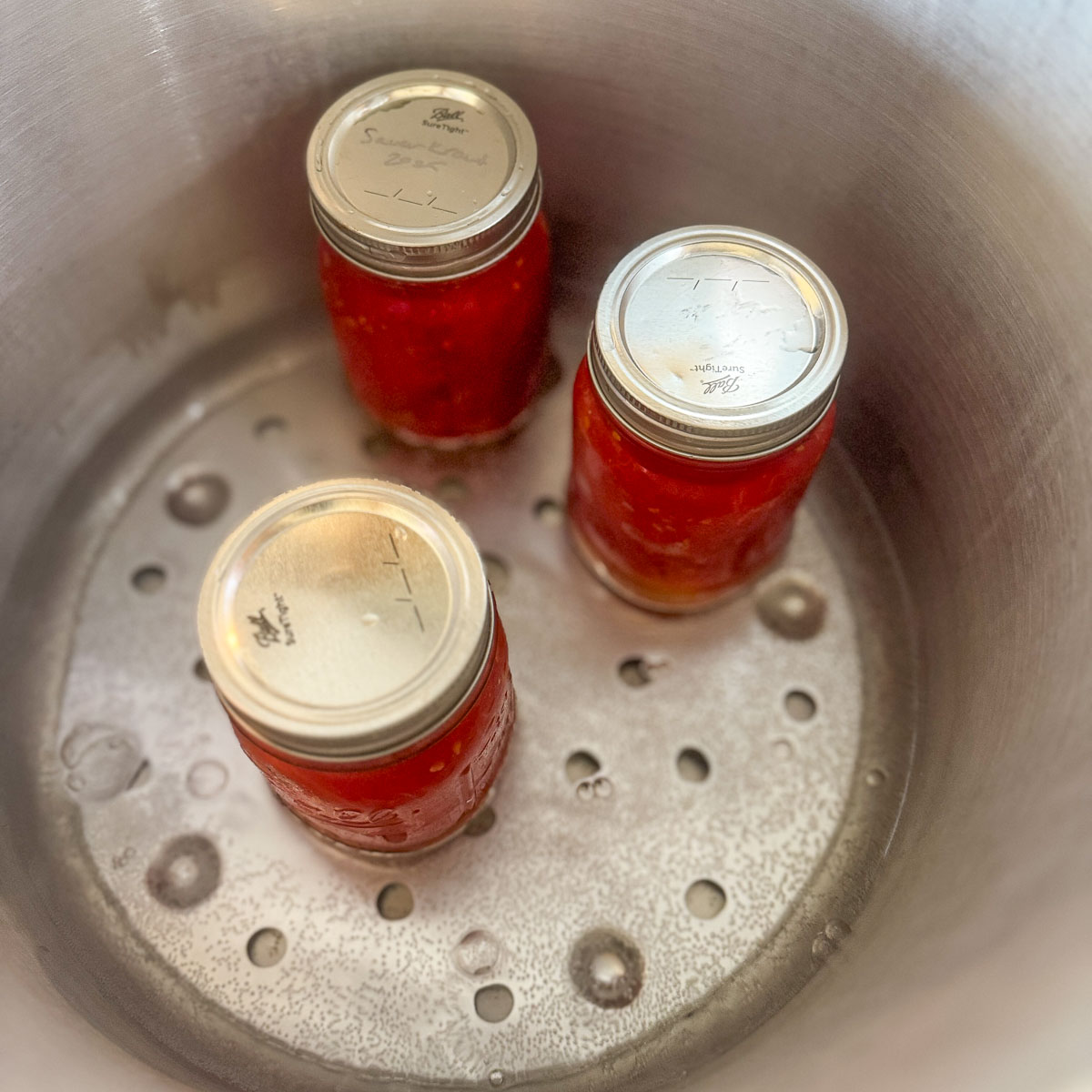 3 mason jars of tomatoes in a pressure canner