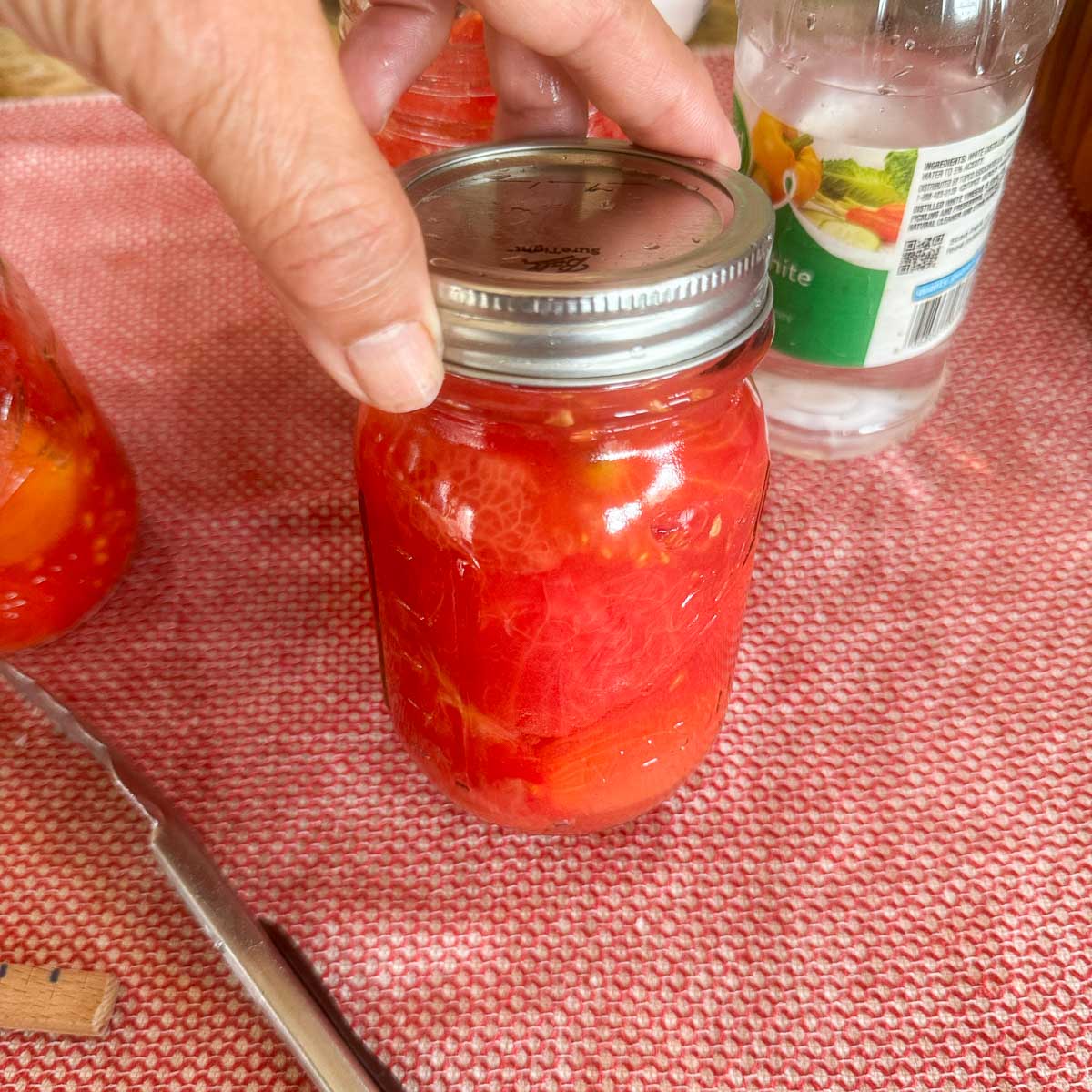 tightening the lid on mason jar full of tomatoes