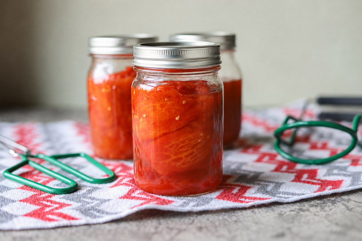 3 jars of pressure canned tomatoes on a towel with some canning tools next to them.