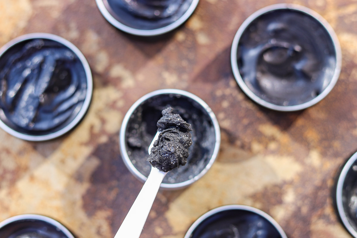 black drawing salve in tins with a white plastic spoon in one of them.