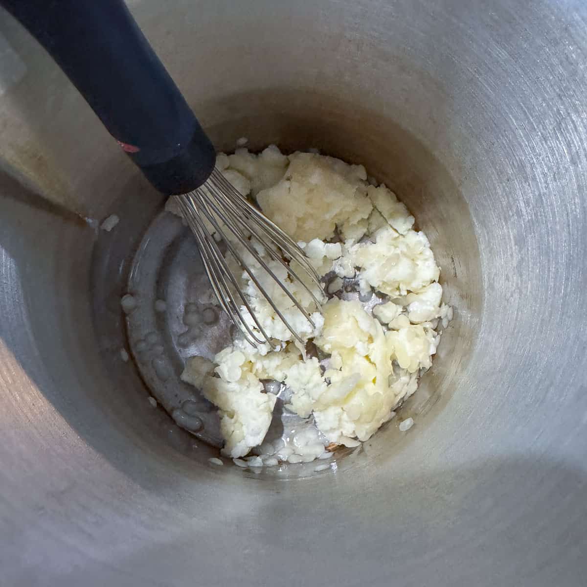 wax pellets and tallow in a pot with a whisk