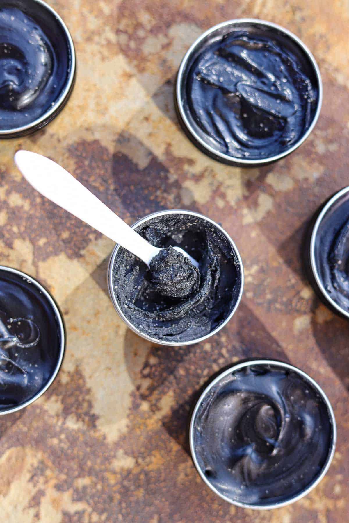 tins of black drawing salve with a white plastic spatula in one of them