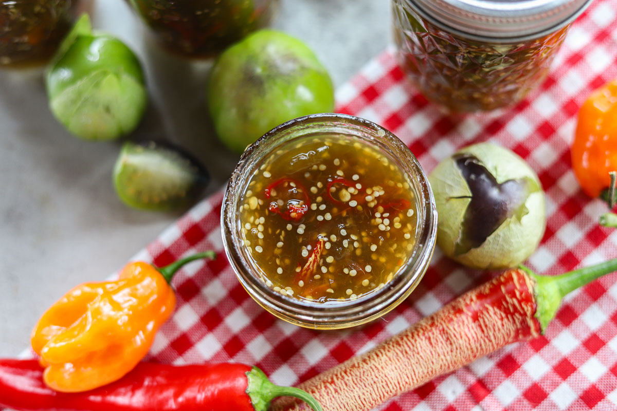 spicy purple tomatillo jam  in a jar with peppers and tomatillos around it