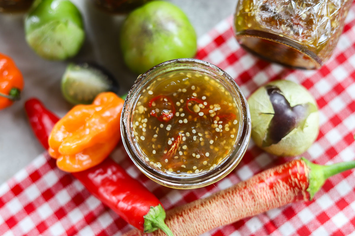 spicy purple tomatillo jam in a jar with peppers and tomatillos around it