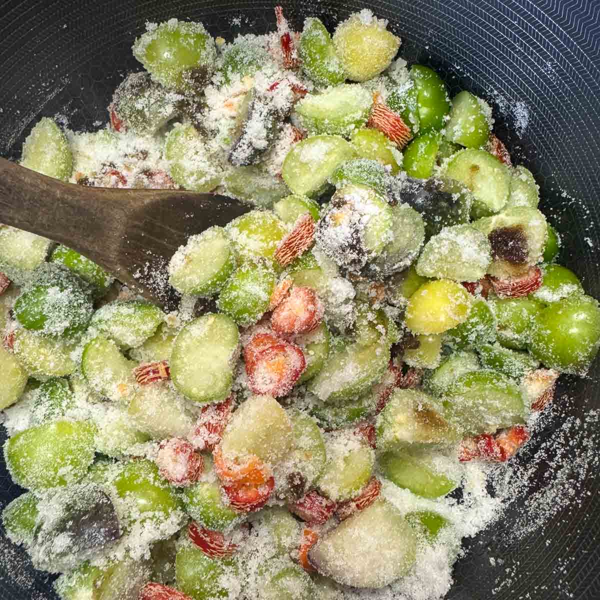 chopped tomatillos and sugar in a pot being stirred with a wooden spoon